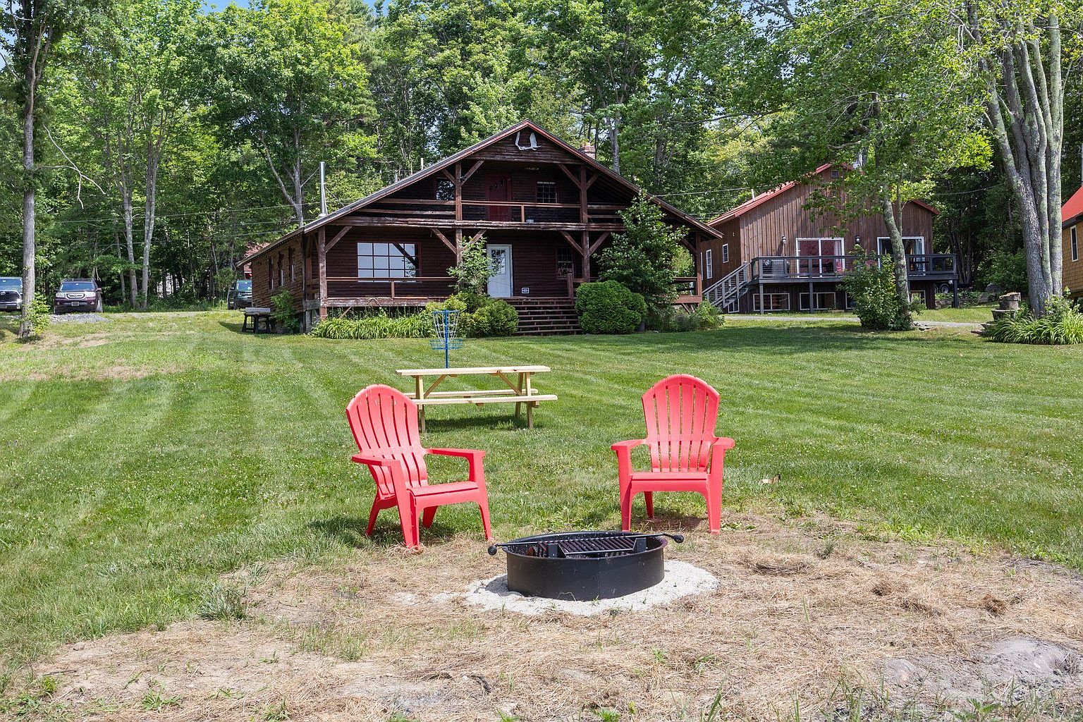 Two red Adirondack chairs and a fire ring on the lawn in front of the central lodge in summer light.
