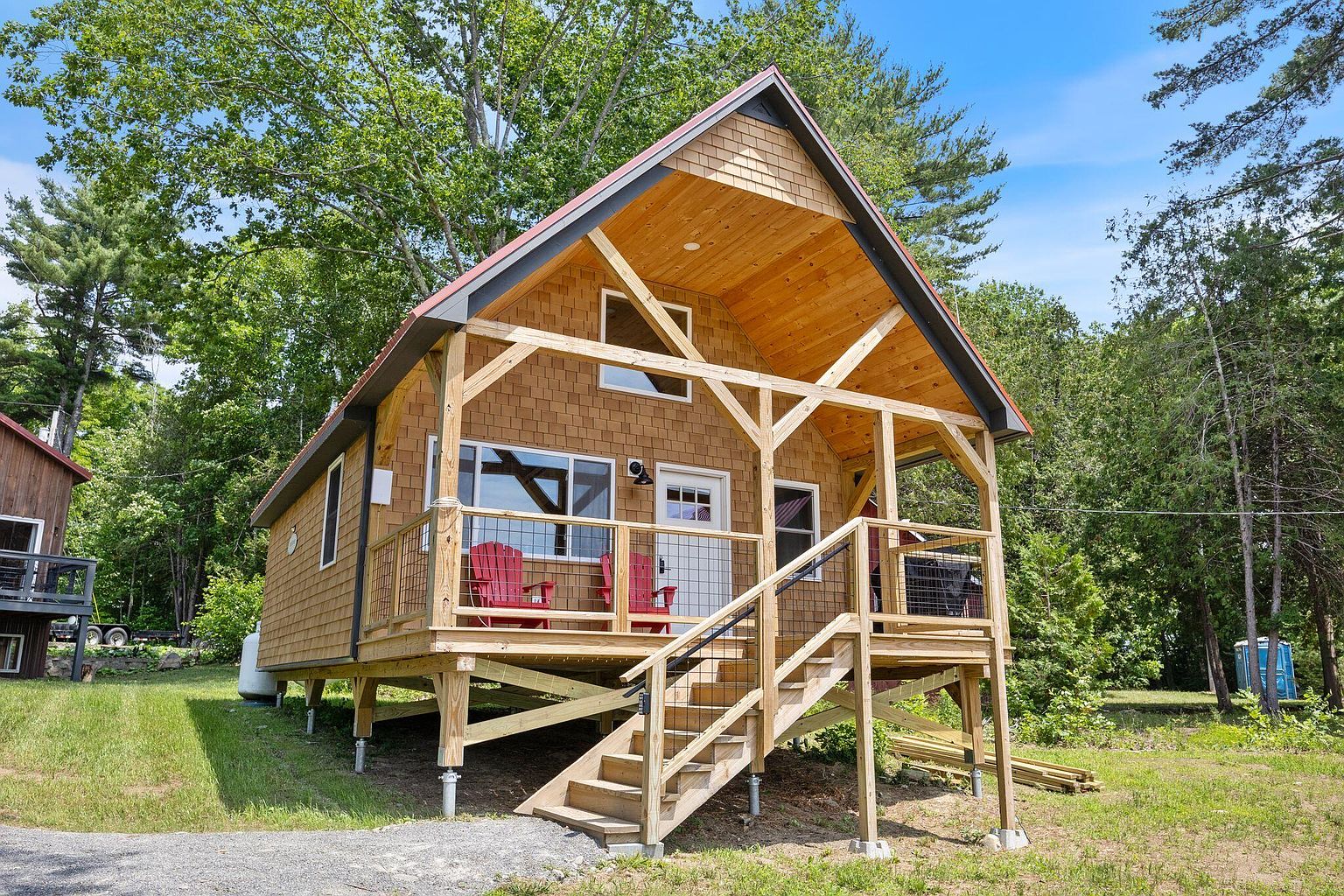 A single cedar-shingle cabin with red Adirondack chairs on the porch, set against tall pines.