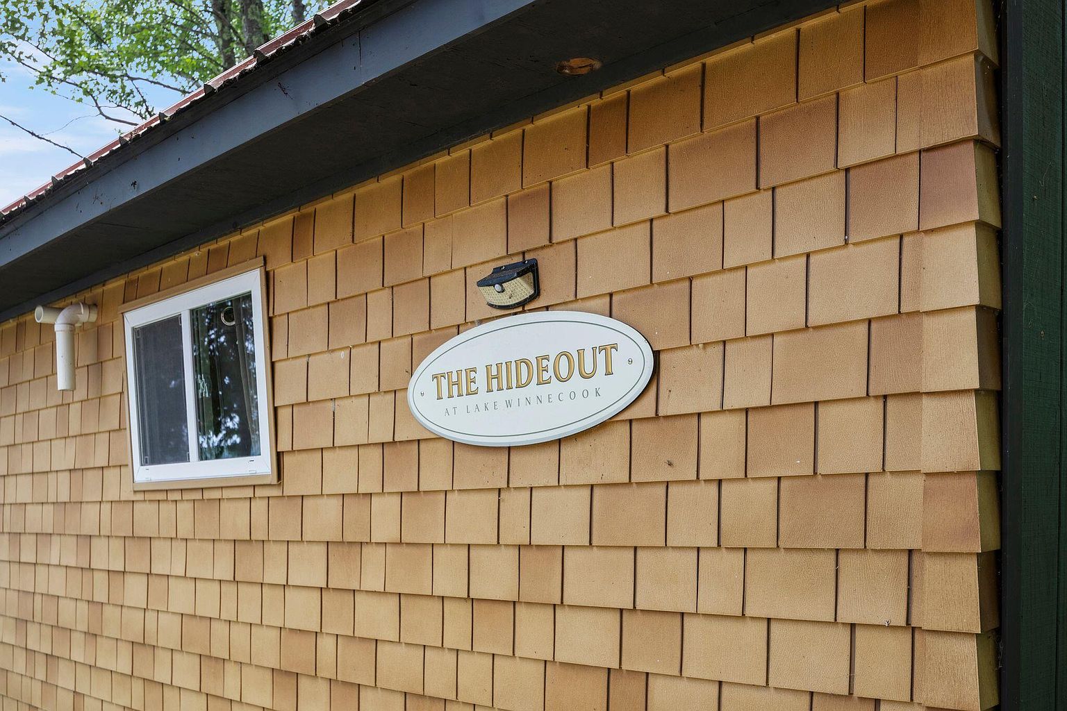 Exterior of The Hideout, a cedar-shingle cabin with a small oval name plaque, late spring light.