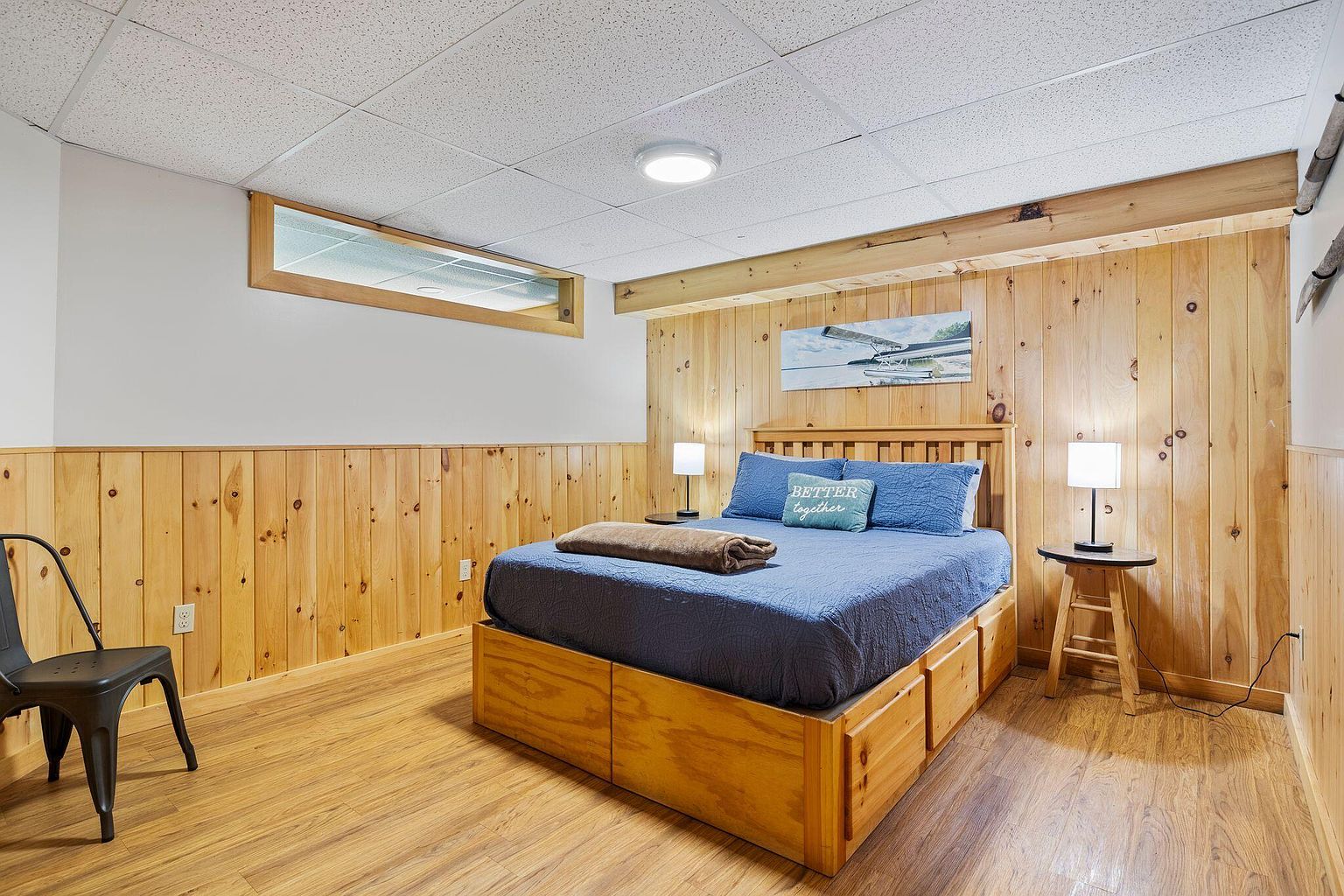 Cabin bedroom with knotty pine wainscoting, a queen bed dressed in deep blue, soft Maine morning light.