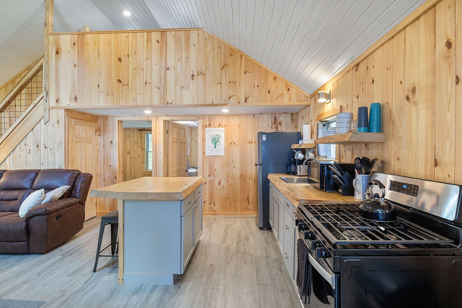 The Retreat cabin photographed from the lakeside, with picnic table and two Adirondack chairs at the water's edge.